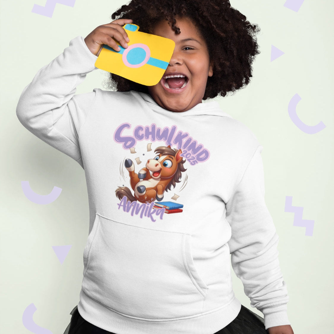 personalisierter Kinderpullover zur Einschulung. Aufdruck "Schulkind 2025" und dein Wunschname. Süßes Pony das auf einem Stapel Bücher sitzt.