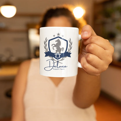 Frau hält Tasse mit Aufdruck ‚TT Deluxe Support Team‘ für Turnierreiter in die Kamera – idealer Begleiter für jedes Reitturnier, hochwertiges Design für Reiter und Pferdefans Keramiktasse mit TT Aufdruck und Pferdewappen Motiv