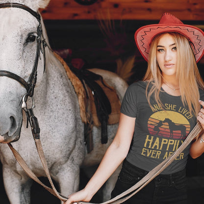 Frau und Pferd stehen vor dem Stalltrakt mit ihrem Pferd. Die Frau trägt ein Pferdeshirt für Damen, Figurbetont mit Pferdemotiv "Happily ever after"  