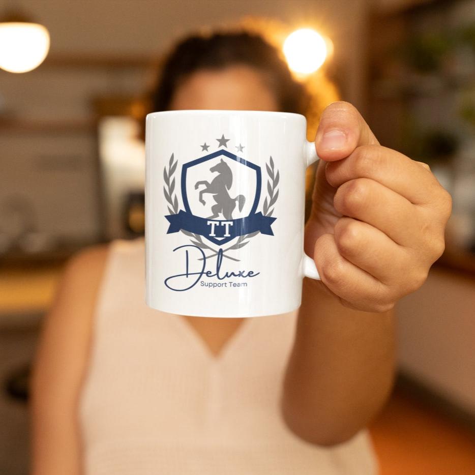 Frau hält Tasse mit Aufdruck ‚TT Deluxe Support Team‘ für Turnierreiter in die Kamera – idealer Begleiter für jedes Reitturnier, hochwertiges Design für Reiter und Pferdefans Keramiktasse mit TT Aufdruck und Pferdewappen Motiv